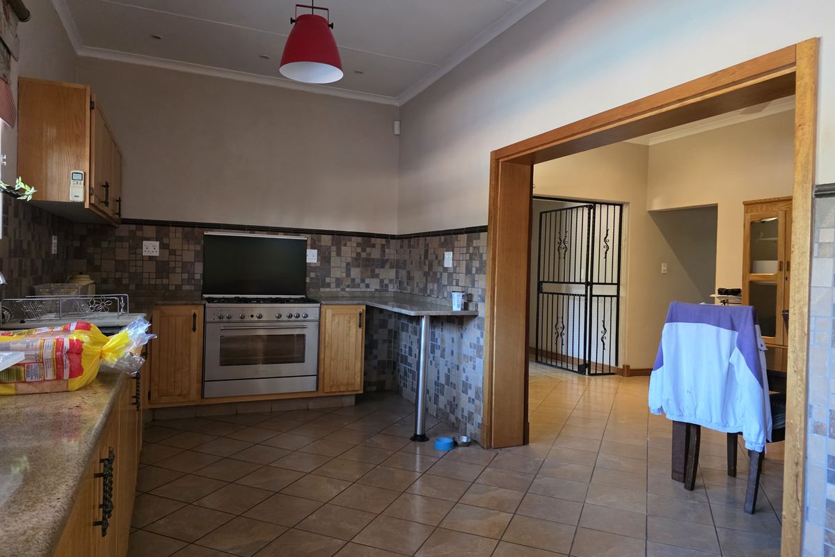 A functional kitchen featuring wooden cabinetry, granite countertops, a built-in oven with hob, and tiled flooring, leading into an adjacent living area.
