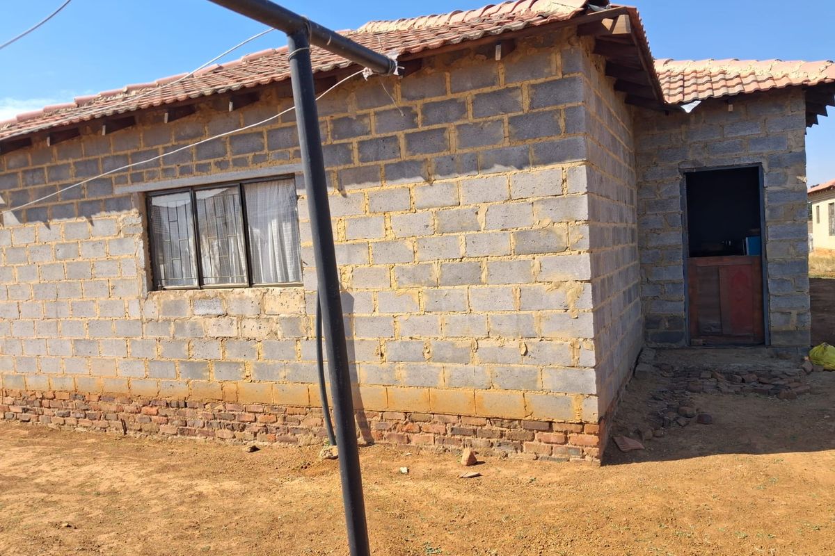 Exterior view of a single-story house featuring unfinished concrete block walls, a tiled roof, and a simple entrance doorway.