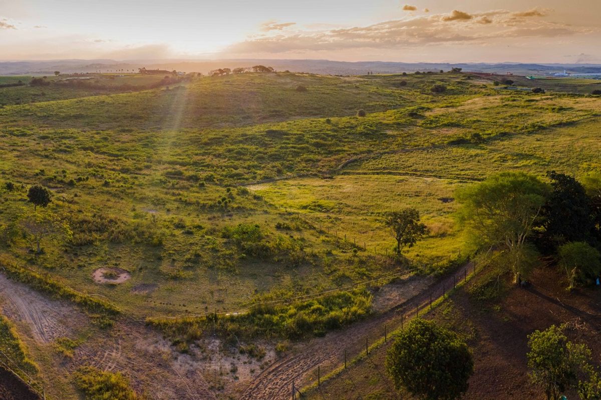 An expansive aerial view of open rural land featuring rolling hills, natural vegetation, and perimeter fencing at sunset.