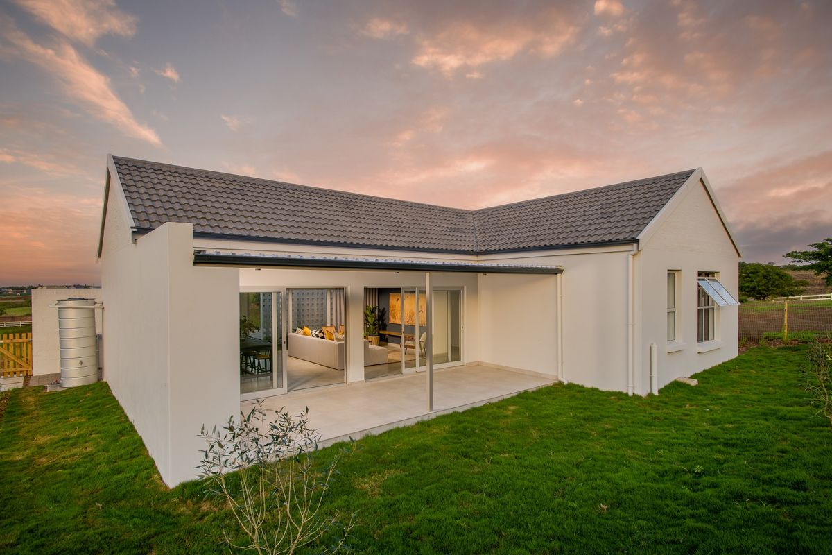 Rear view of a modern house featuring a covered patio, sliding glass doors, and a well-maintained lawn at sunset.