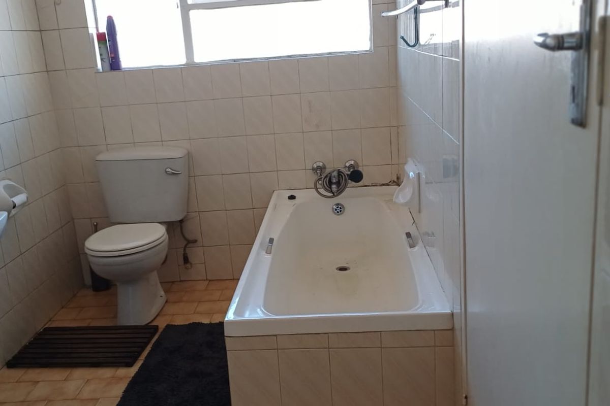 A dated bathroom featuring a standard bathtub, pedestal basin, and toilet with original wall tiling and ceramic floor tiles.