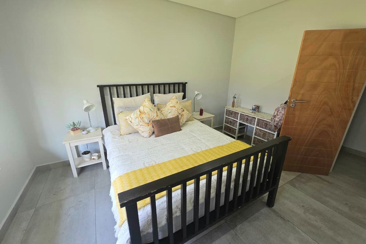 A well-maintained bedroom featuring neutral wall tones, large format floor tiles, and a solid wood interior door.