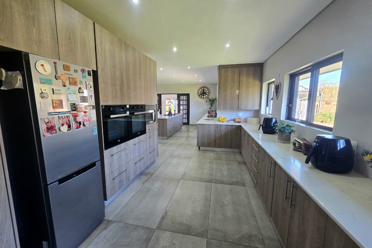Modern kitchen featuring wood-grain cabinetry, stone countertops, integrated double ovens, and large format floor tiles, with an open-plan layout leading to adjacent living areas.