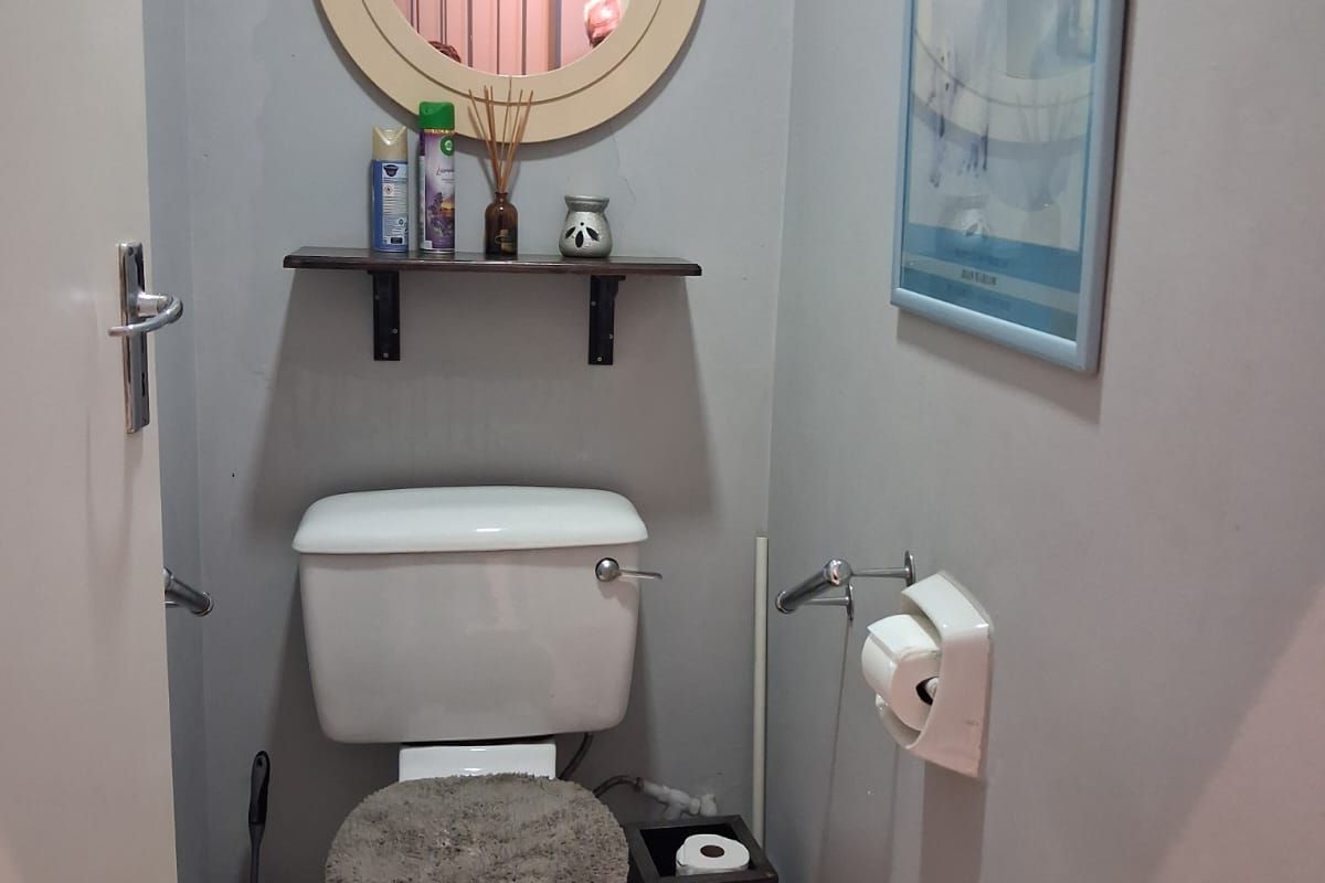 A compact guest bathroom featuring a standard toilet, wall-mounted mirror, and tiled flooring.
