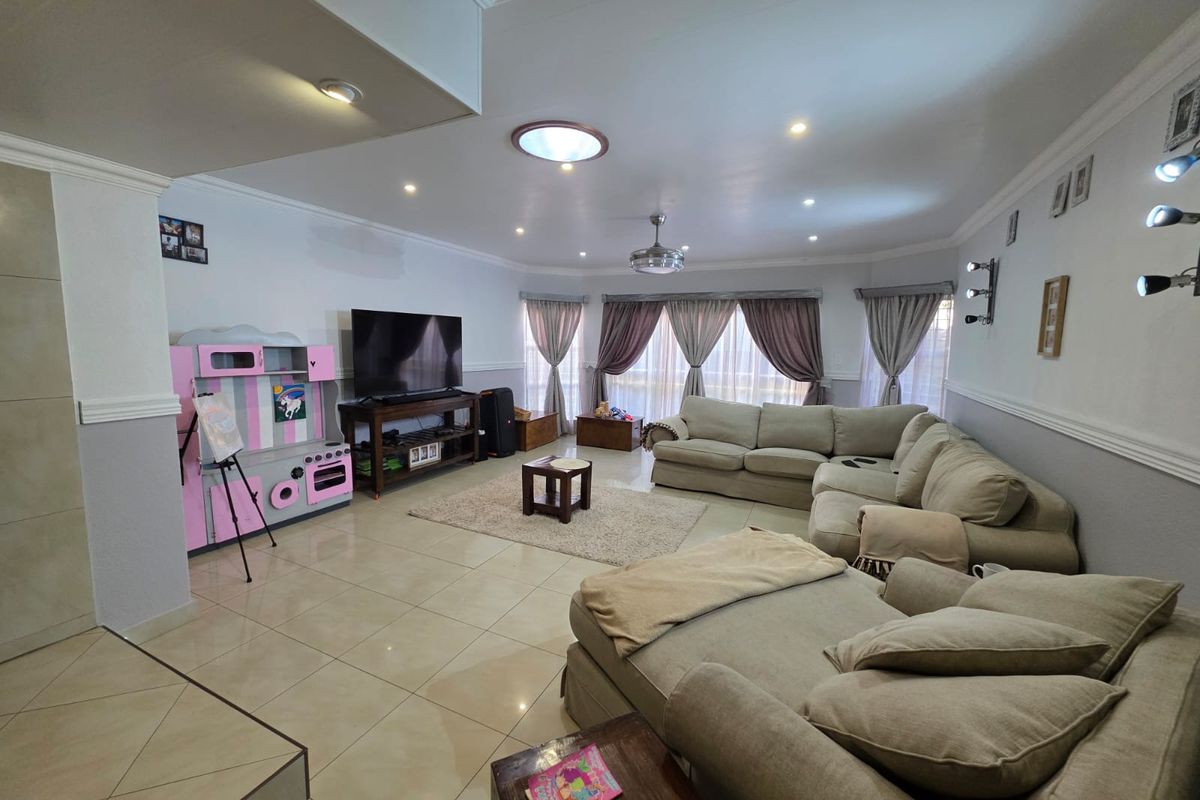 Spacious open-plan living area featuring large format floor tiles, recessed downlighting, a ceiling fan, and expansive windows with draped curtains.