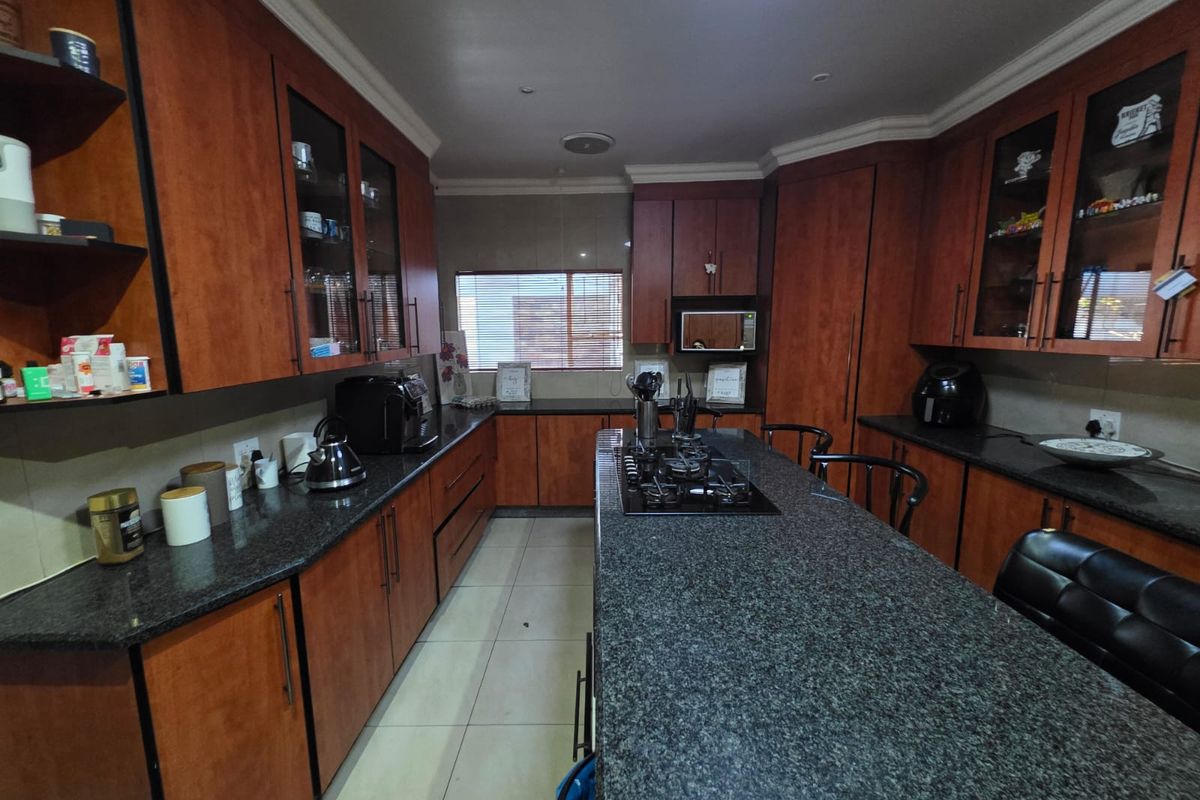 Spacious kitchen featuring dark granite countertops, extensive cherry wood cabinetry, a central island with a built-in gas hob, and tiled flooring.