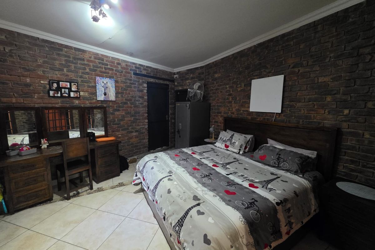 A bedroom featuring exposed brick feature walls, tiled flooring, and a ceiling-mounted light fixture.