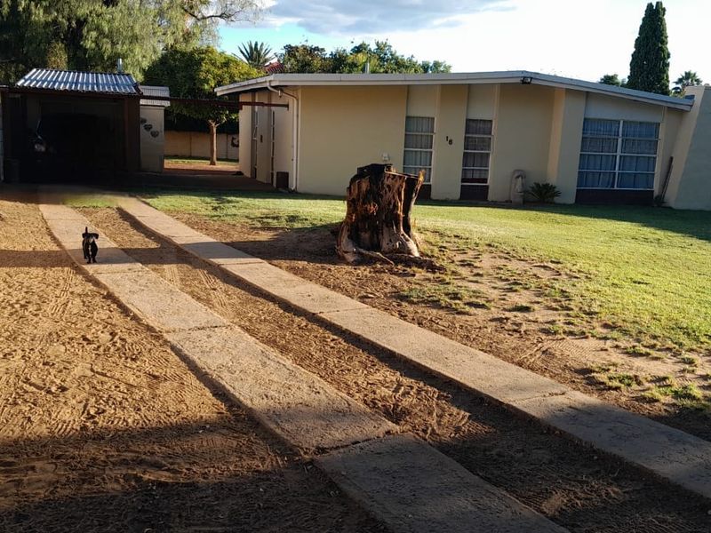 A view of the rear exterior of the house featuring a concrete driveway, lawn area, and a detached garage structure.