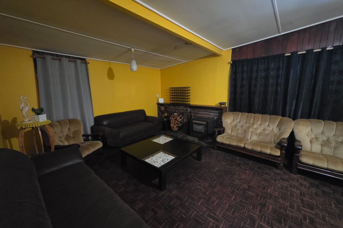 A living room featuring a brick fireplace, wood-look flooring, and yellow walls, offering a dated aesthetic ready for modernization.