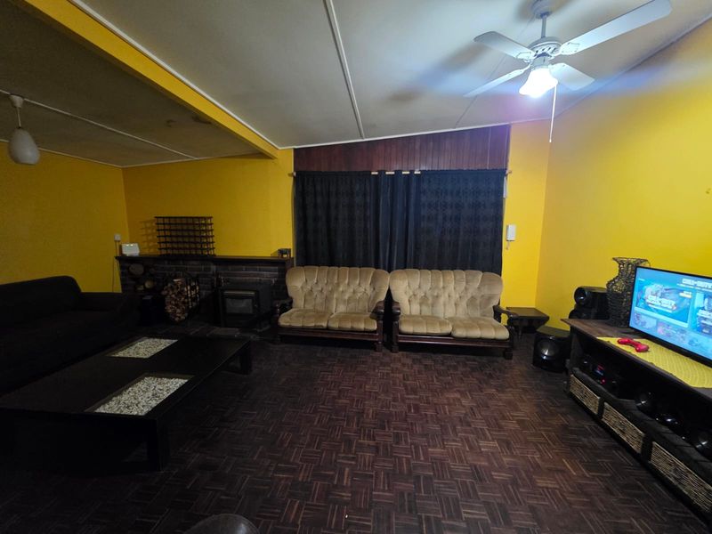 Spacious living room featuring dark parquet flooring, a built-in brick fireplace, and a ceiling fan, offering a traditional layout with potential for modernization.