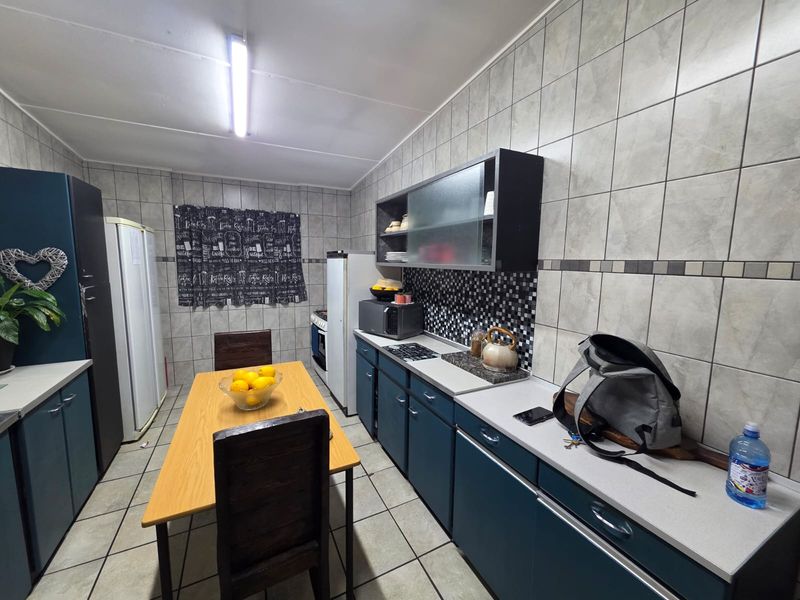 A functional kitchen featuring dark blue cabinetry, light countertops, tiled walls, and a dedicated dining area with tiled flooring.