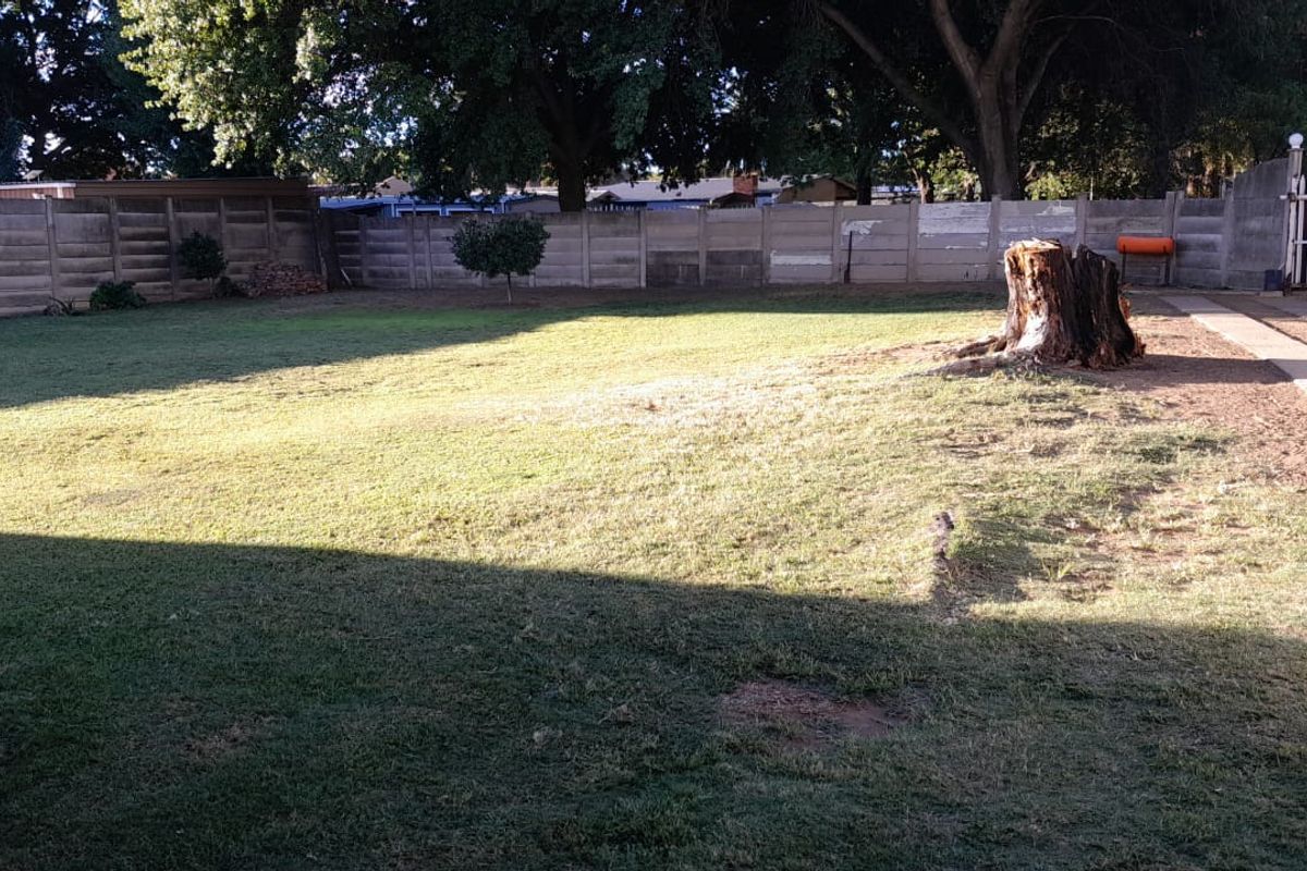 A spacious rear garden featuring a large lawn area, enclosed by a concrete boundary wall and a white picket gate.