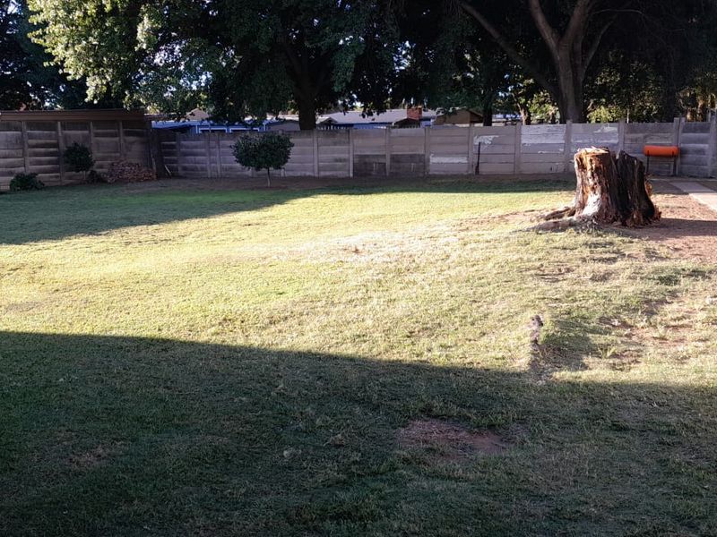 A spacious rear garden featuring a large lawn area, enclosed by a concrete boundary wall and a white picket gate.