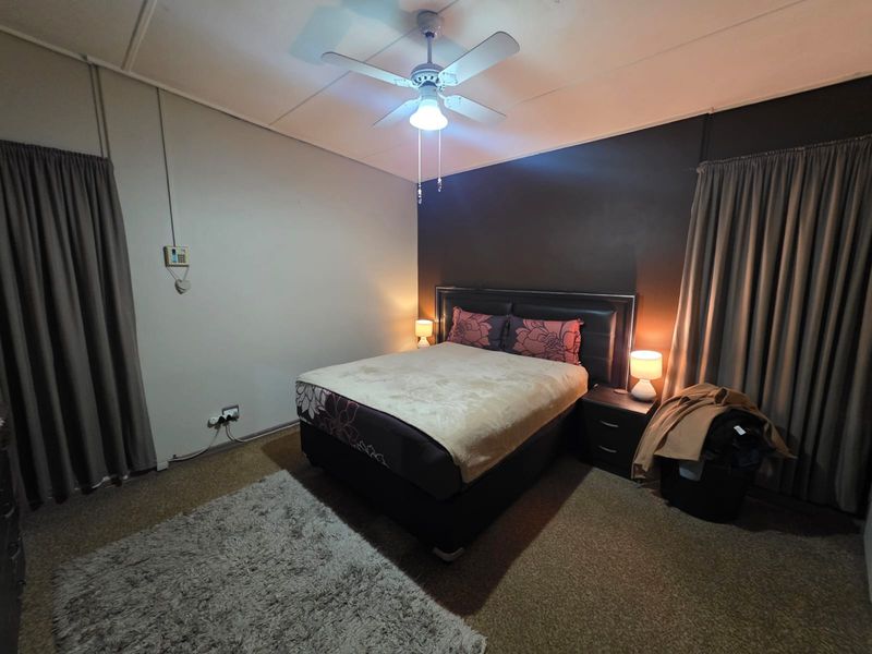 A bedroom featuring a ceiling fan, neutral wall finishes, and carpeted flooring, providing a functional space for rest.