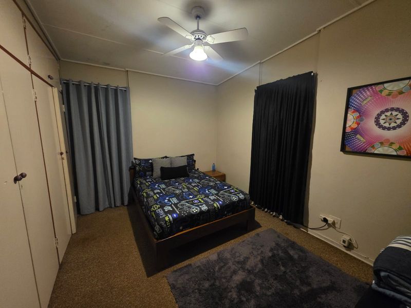 A functional bedroom featuring built-in storage cabinetry, a ceiling fan, and neutral wall finishes.