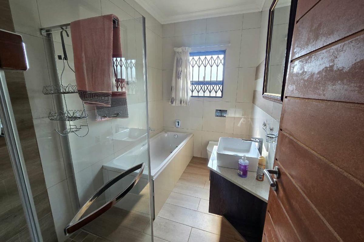 A modern bathroom featuring a glass-enclosed shower, a built-in bathtub, a vanity basin, and tiled flooring with security bars on the window.