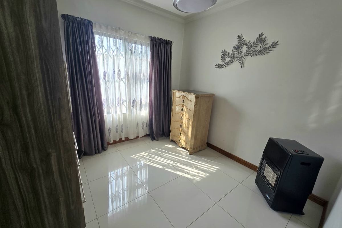A bright bedroom featuring polished porcelain floor tiles, a built-in wardrobe, and a window fitted with a security gate.