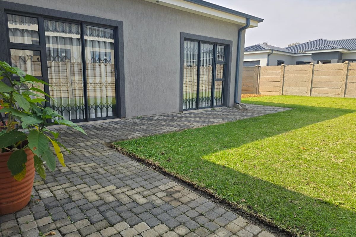 Rear view of the property featuring a paved patio area, sliding glass doors with security gates, and a well-maintained lawn with perimeter walling.