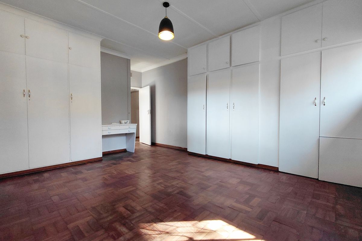 Spacious bedroom featuring extensive built-in cabinetry, classic parquet flooring, and a neutral color palette, offering a clean and functional living space.