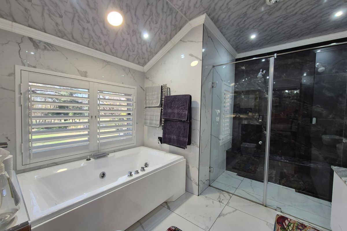 Modern bathroom featuring a built-in soaking tub, a glass-enclosed walk-in shower, marble-style wall and ceiling tiles, and plantation shutters.