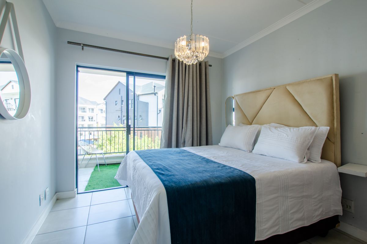 A well-lit bedroom featuring tiled flooring, a built-in headboard, and sliding glass doors that open onto a private balcony.