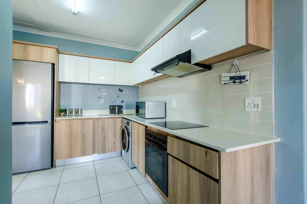 Modern kitchen featuring wood-grain cabinetry, white high-gloss upper cupboards, integrated oven, hob, extractor fan, and space for a washing machine.