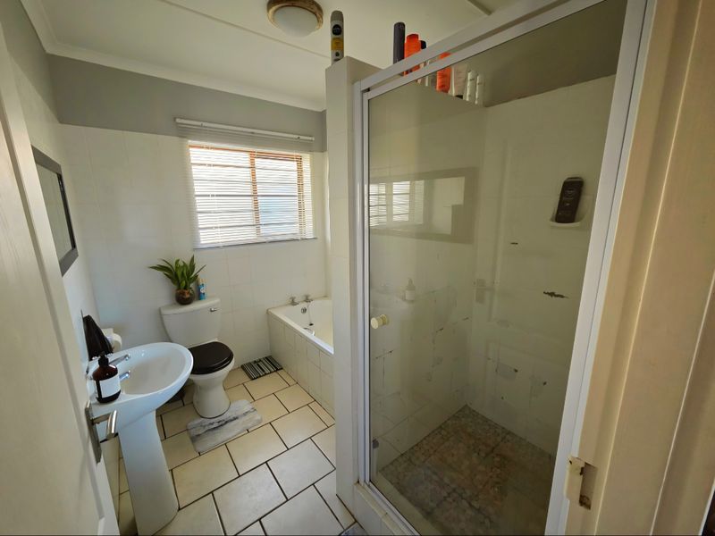 A functional bathroom featuring a pedestal basin, toilet, built-in bathtub, and a separate shower enclosure with tiled flooring.