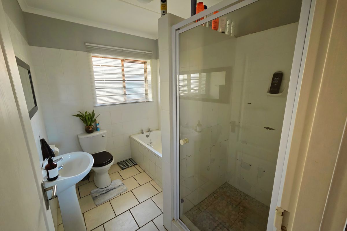 A functional bathroom featuring a pedestal basin, toilet, built-in bathtub, and a separate shower enclosure with tiled flooring.