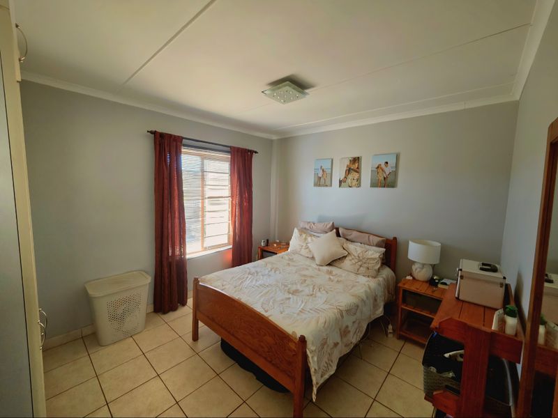 A well-lit bedroom featuring tiled flooring, a built-in wardrobe, and a window with curtain treatments.