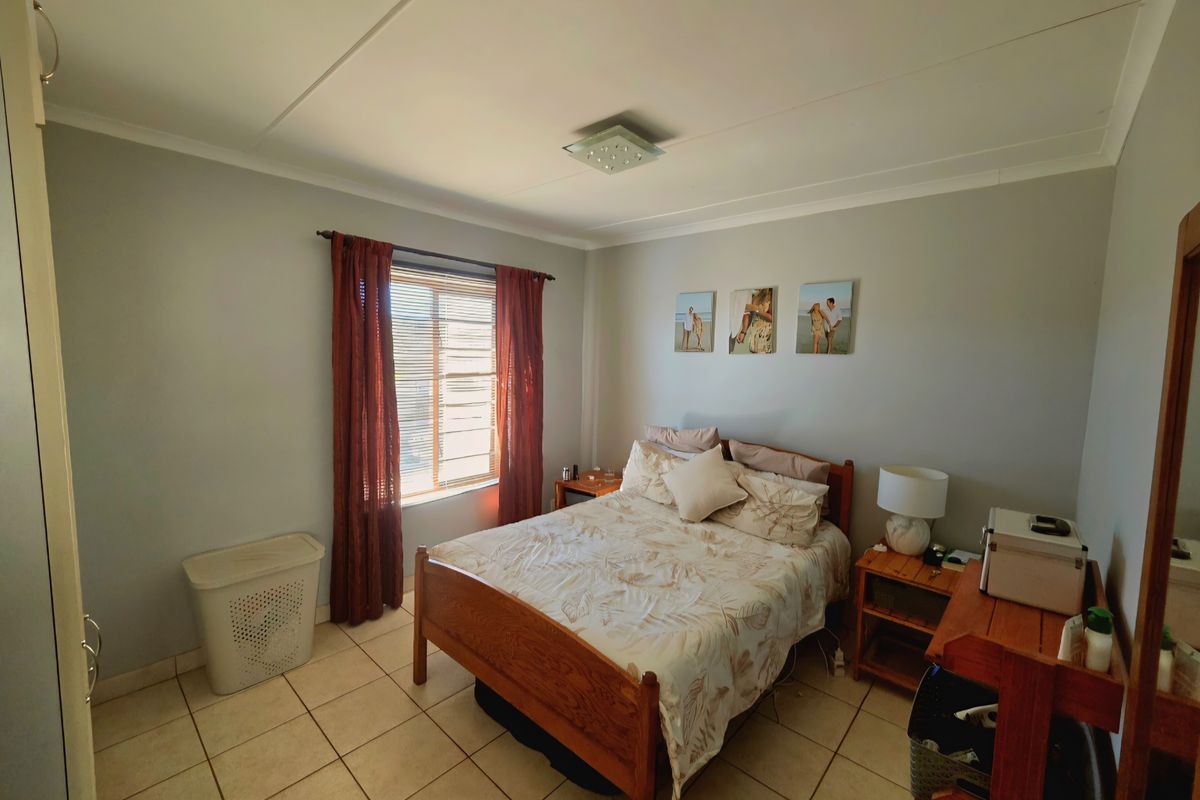 A well-lit bedroom featuring tiled flooring, a built-in wardrobe, and a window with curtain treatments.