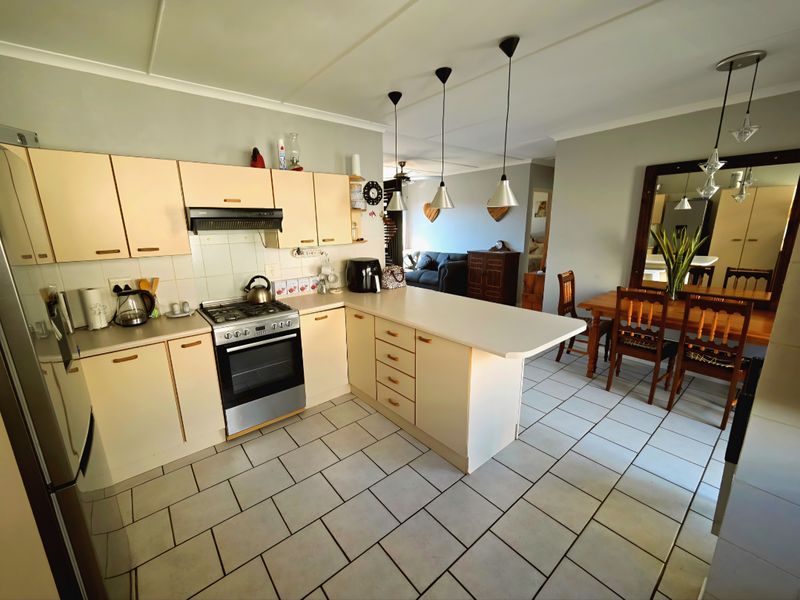 Open-plan kitchen and dining area featuring light-toned cabinetry, a built-in oven with extractor fan, breakfast counter, and tiled flooring throughout.