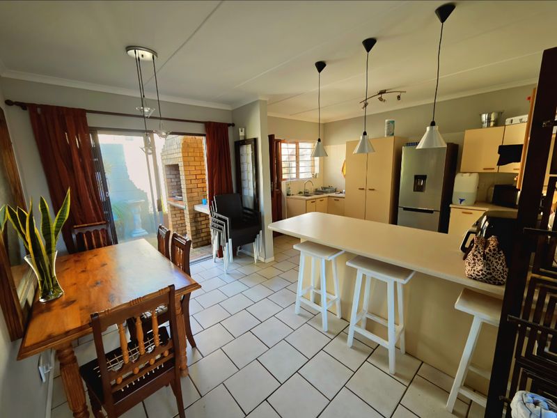 Open-plan kitchen and dining area featuring a breakfast bar, tiled flooring, and direct access to an outdoor patio with a built-in brick braai.