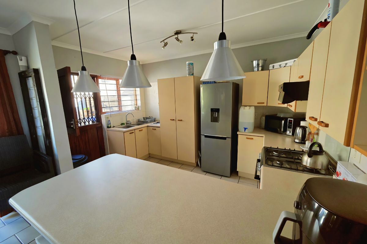 A functional kitchen featuring light-toned cabinetry, a gas hob, stainless steel sink, and a breakfast bar island with pendant lighting.