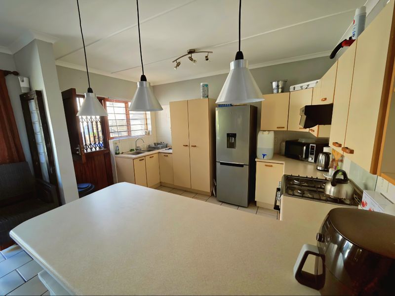 A functional kitchen featuring light-toned cabinetry, a gas hob, stainless steel sink, and a breakfast bar island with pendant lighting.