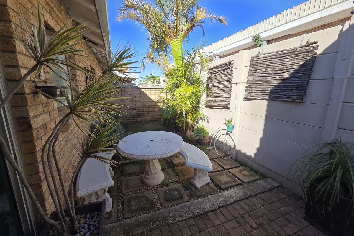 A private rear courtyard featuring a paved patio area, brick boundary walls, and established garden landscaping.