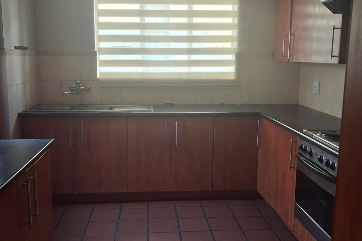 A functional kitchen featuring wood-look cabinetry, dark countertops, a built-in oven with extractor fan, and tiled flooring.