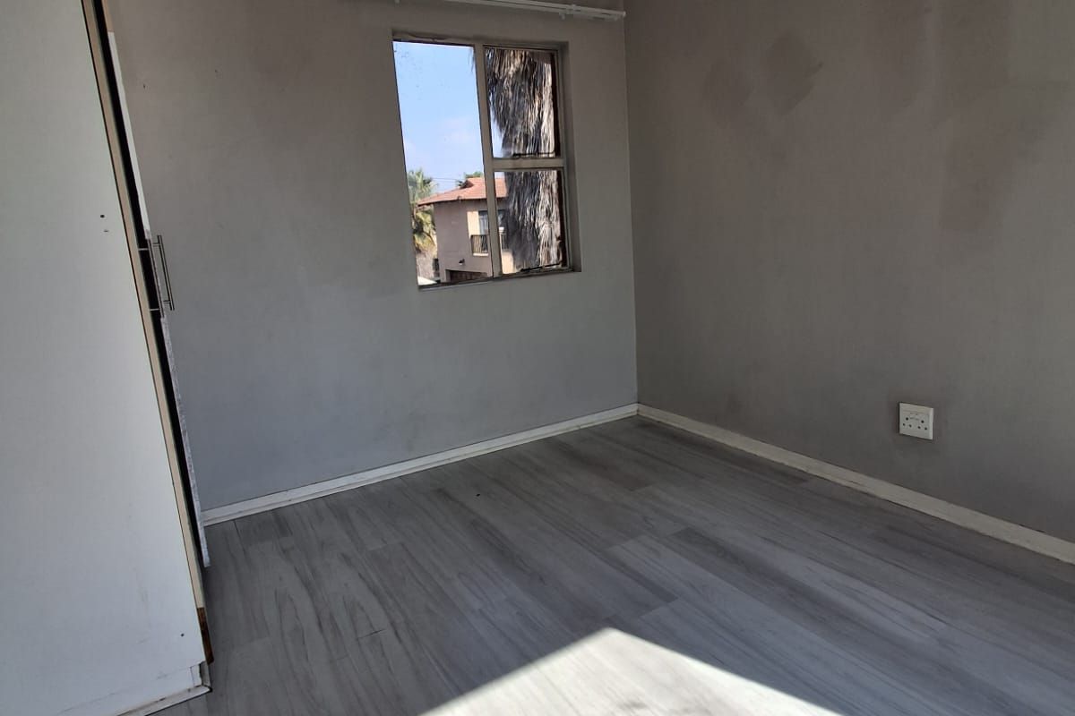 A vacant bedroom featuring light-toned laminate flooring, built-in cupboards, and a single window providing natural light.