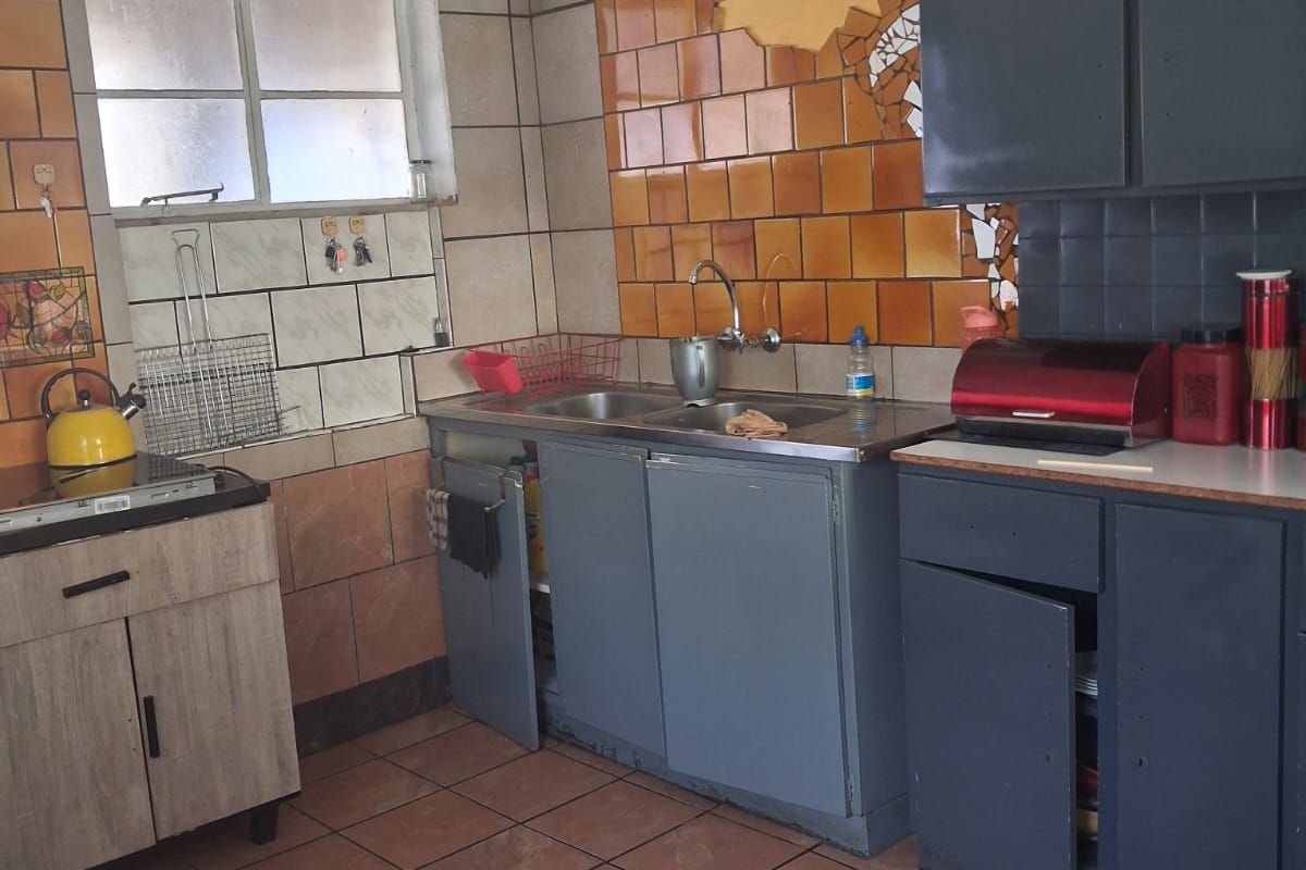 A dated kitchen featuring tiled walls, built-in cabinetry, and a stainless steel sink, requiring significant renovation and cosmetic updates.