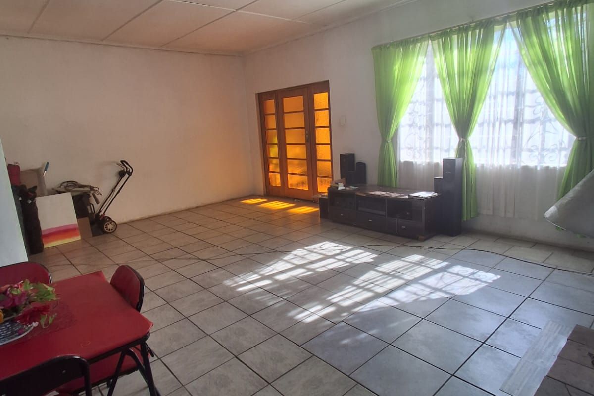 Spacious living area featuring tiled flooring, large windows with natural light, and a wooden framed glass door leading to the exterior.