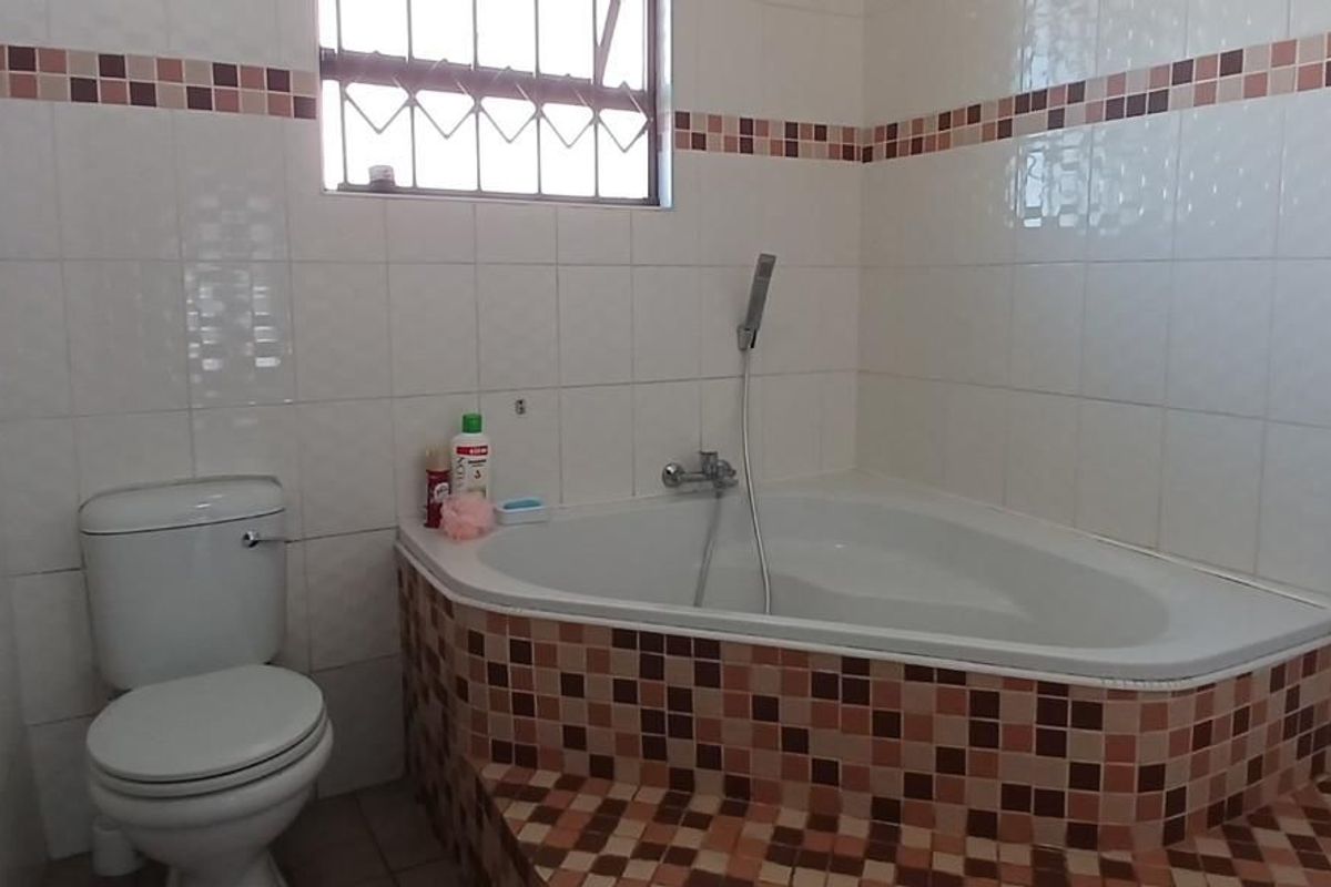 A functional bathroom featuring a corner bathtub with a handheld shower attachment, a standard toilet, and tiled walls with a decorative mosaic border.