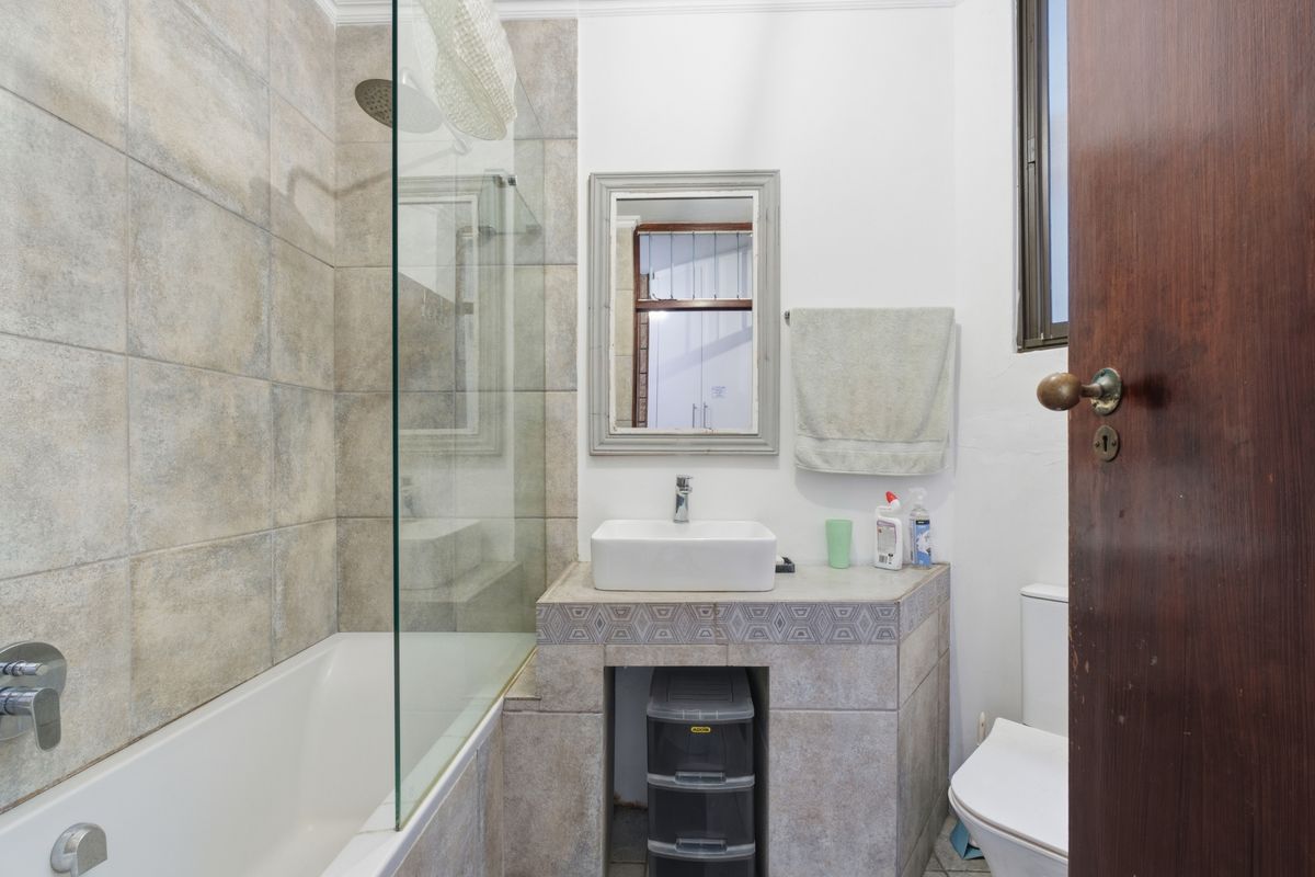 A functional bathroom featuring a tiled bathtub with a glass shower screen, a vessel sink vanity, and a standard toilet.