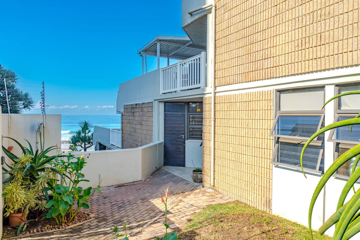 Exterior view of the apartment building featuring brick facade, paved walkway, and a balcony overlooking the ocean.