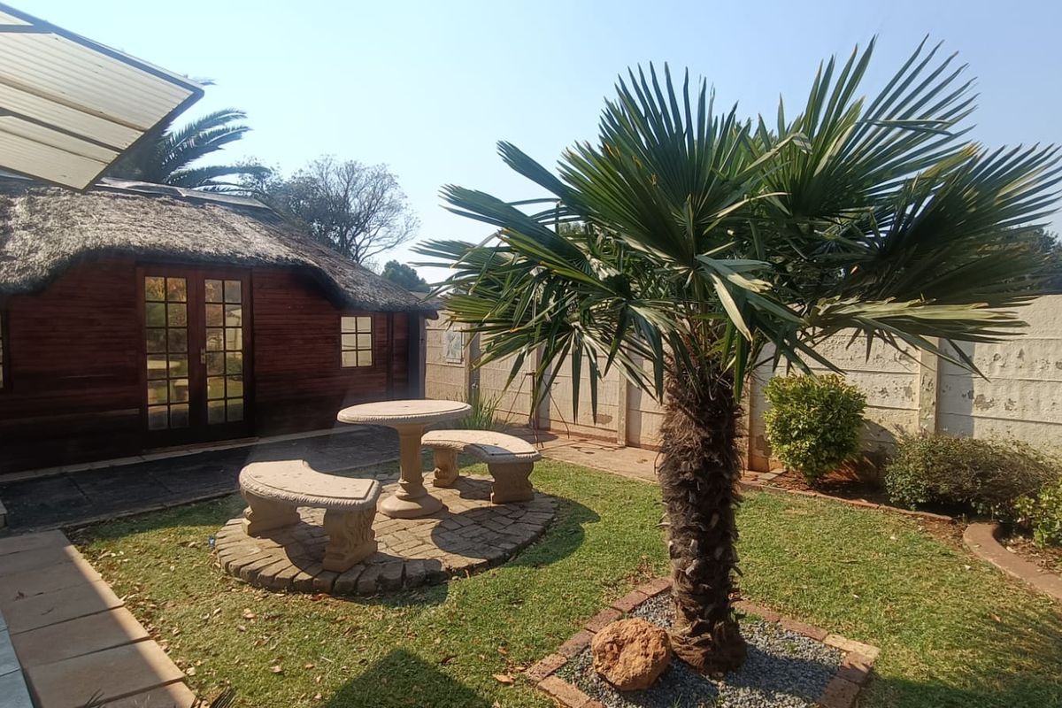 A private rear garden featuring a thatched-roof structure, paved seating area, and established palm tree, offering a tranquil outdoor space.