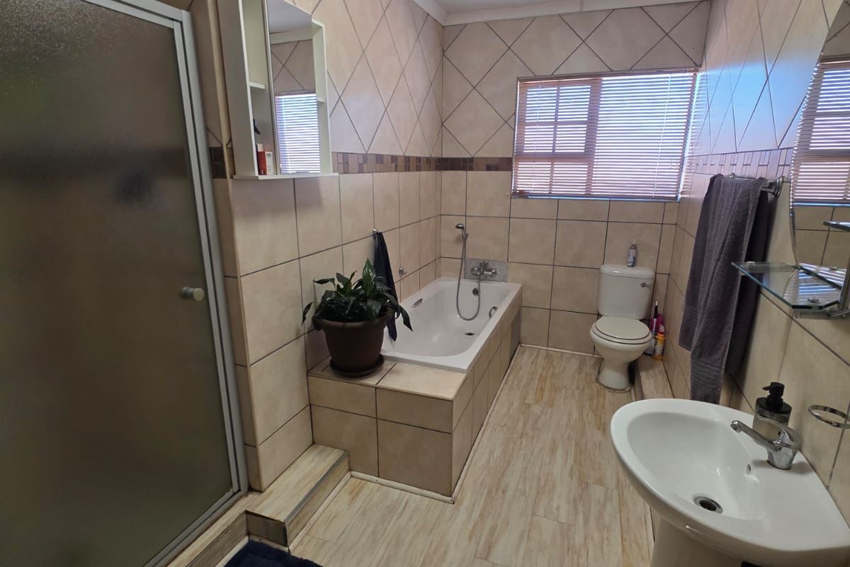 A functional bathroom featuring a tiled shower enclosure, a built-in bathtub, a pedestal basin, and a toilet with neutral wall and floor tiling.