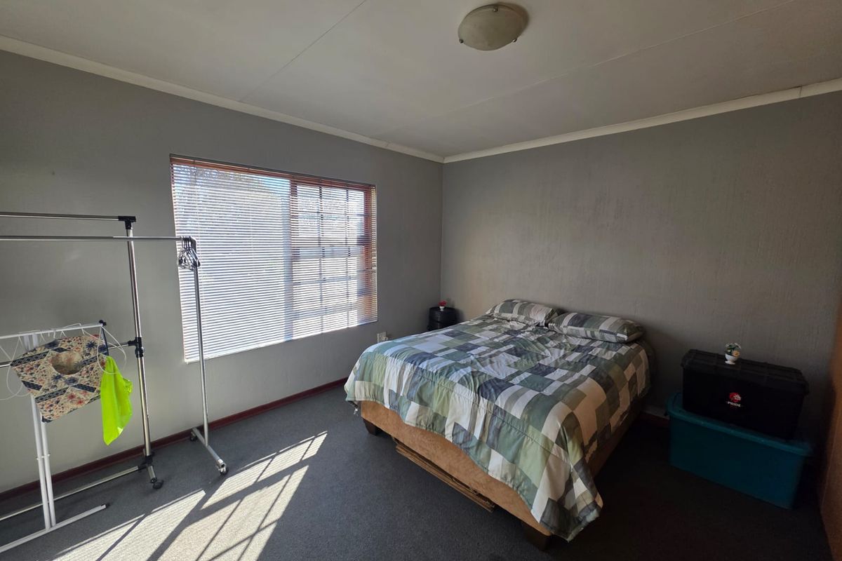 A functional bedroom featuring grey walls, carpeted flooring, and a window fitted with horizontal blinds.