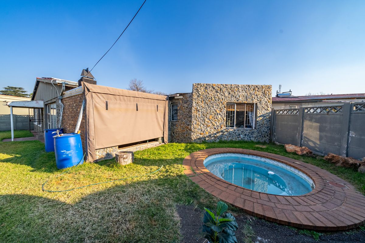 Rear garden area featuring a small oval swimming pool with brick coping, stone-clad exterior wall, and a covered patio space.