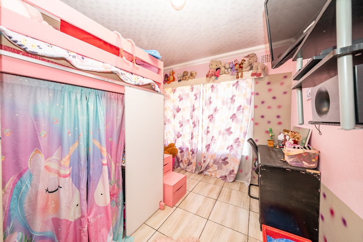 A bedroom featuring tiled flooring and a ceiling rose, currently decorated with vibrant wall finishes and personal items.