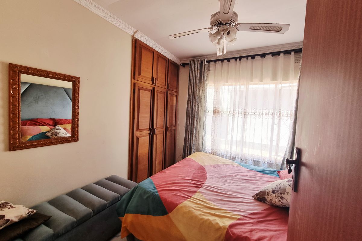 A bedroom featuring built-in wooden cupboards, a ceiling fan, and large windows with curtains, providing a functional and lived-in space.