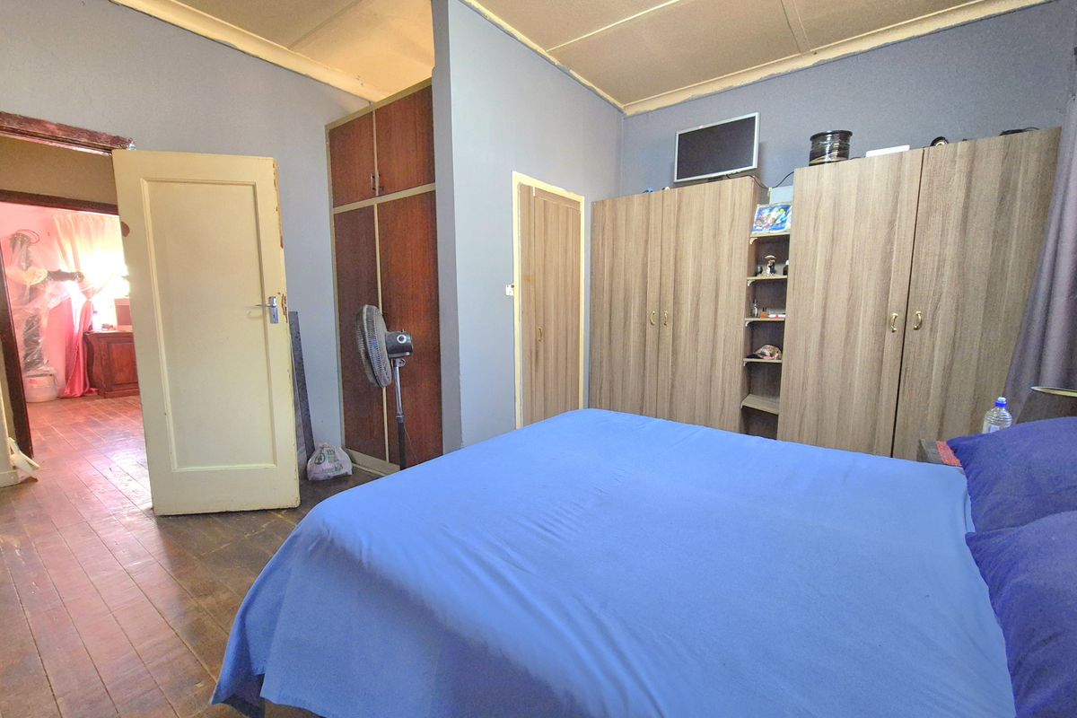 A bedroom featuring built-in wooden wardrobes, timber flooring, and access to an adjacent room.