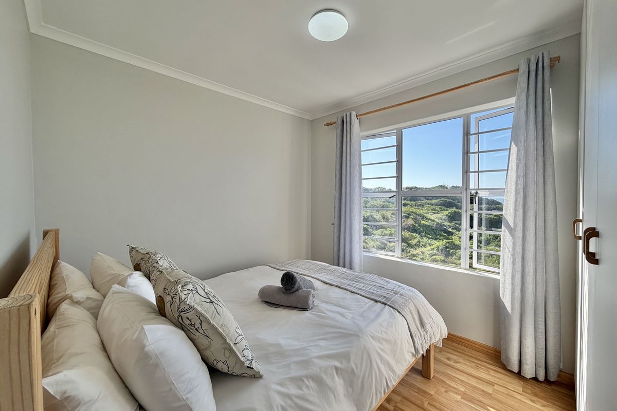 A bright and well-maintained bedroom featuring laminate flooring, a built-in wardrobe, and large windows offering scenic natural views.
